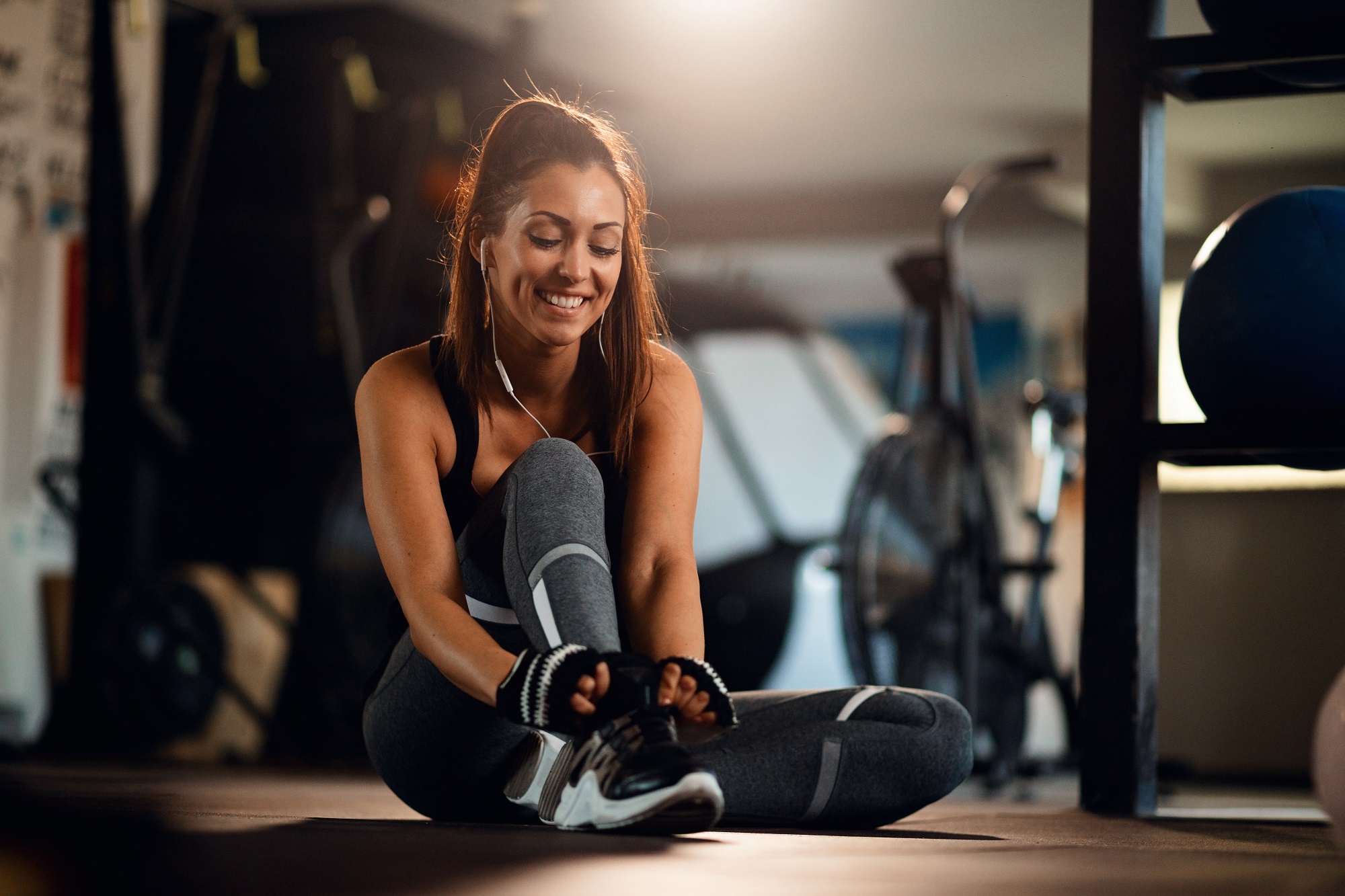 Happy athletic woman tying shoelace while sitting on the floor in a gym. Program personalizat - imagine 1